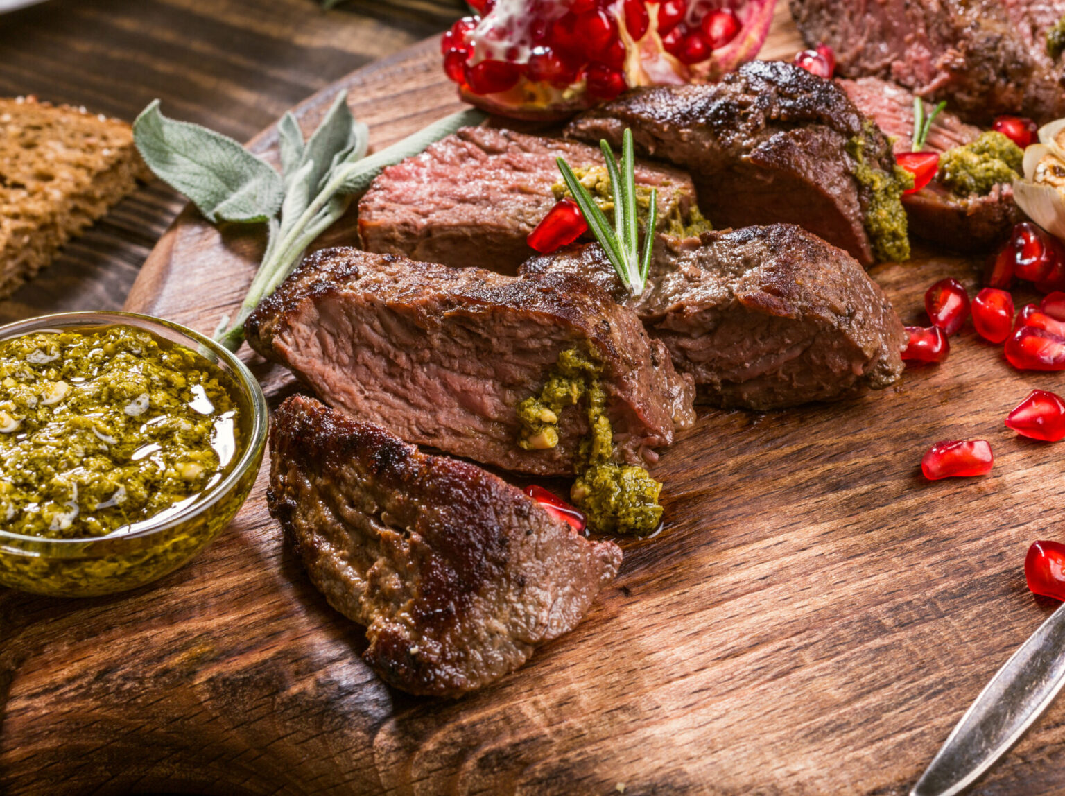 Kangaroo meat steak with green pesto and pomegranate on wooden cutting board. Helthy holiday food concept. Selective focus.