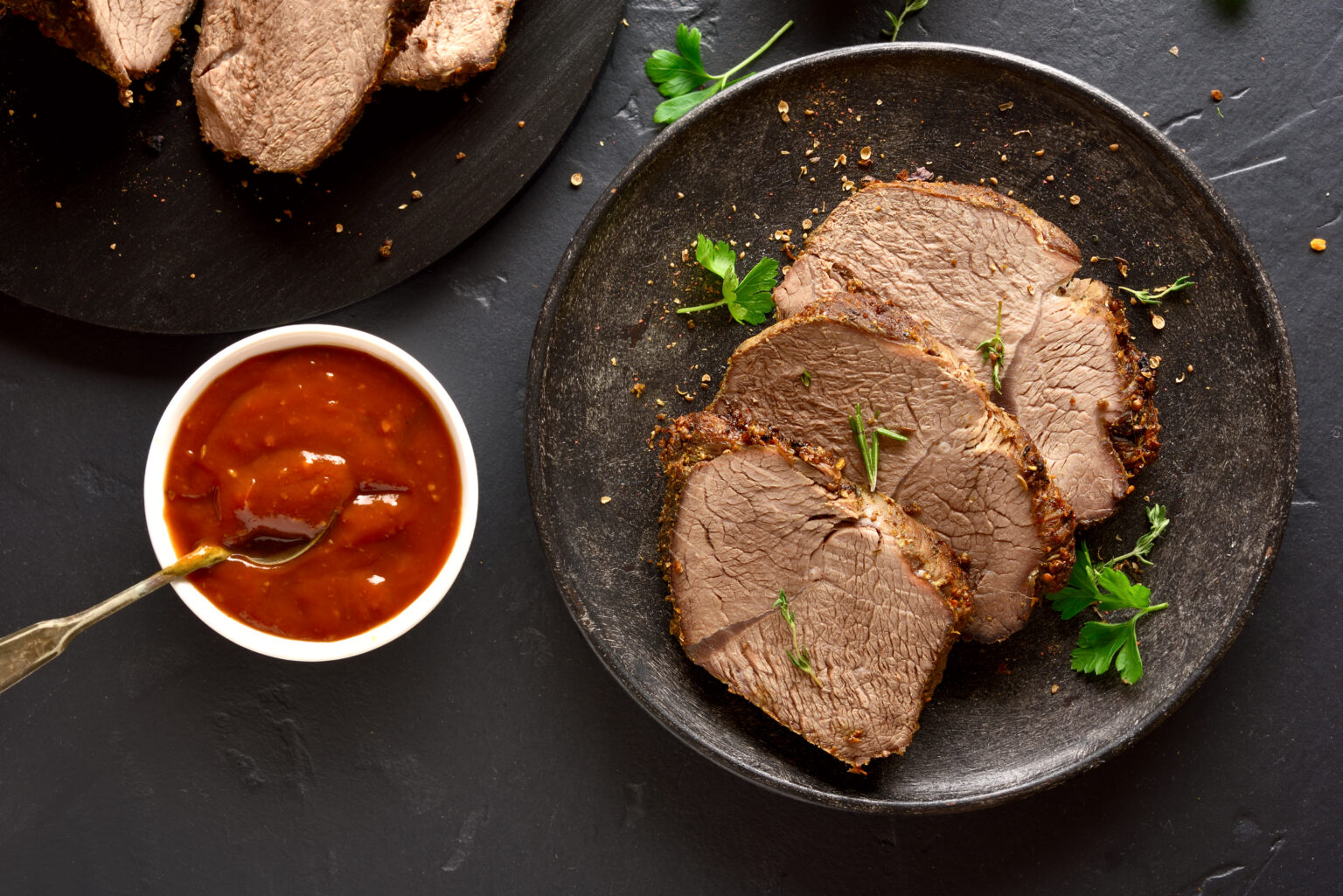 Roasted beef on plate over dark stone background. Tasty cooked beef with sauce. Top view, flat lay