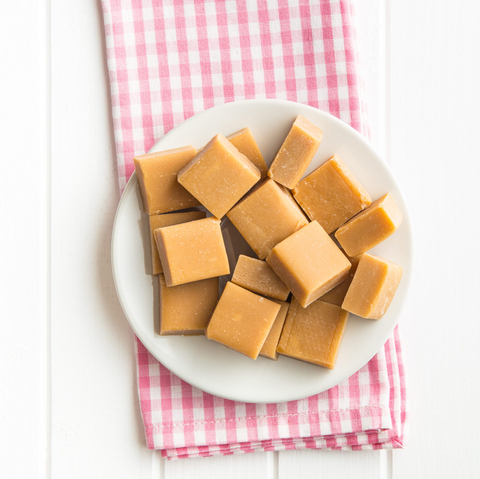 Sweet caramel candies on plate and checkered napkin. Top view.